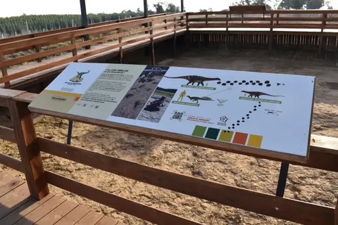 Cartel bilingüe con huellas de dinosaurio, código QR y mapa del sitio, Ruta de los Dinosaurios