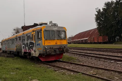 Coche motor de AFE sobre las vías, con una arboleda y vagones de carga al fondo